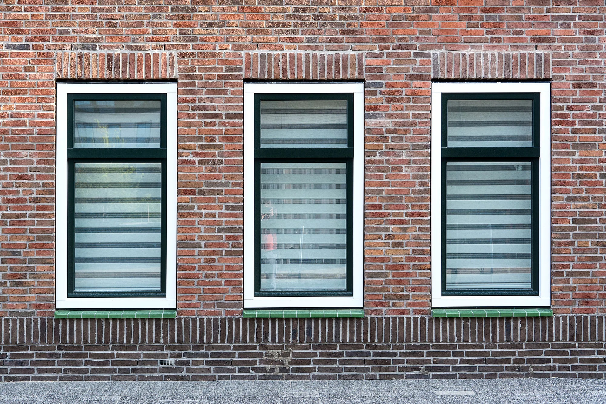 Drie witte kunststof kozijnen met donkergroene binnenkaders in een Nederlandse bakstenen gevel
