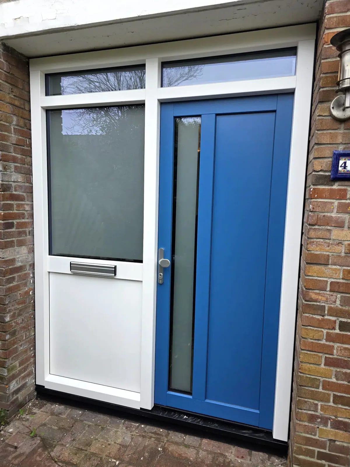 Blauwe kunststof voordeur met wit kader, zijlicht en brievenbus in een bakstenen gevel